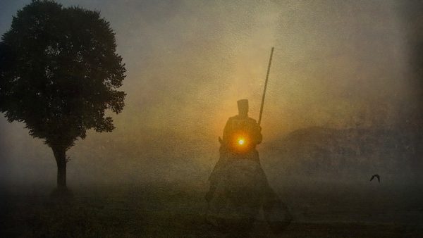 ghostly figure of a knight on a horse at last light of day, near a silhouetted tree