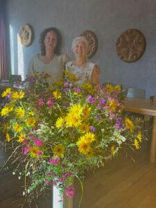 Two women posing for a photo behind a large bunch of spring flowers in a vase