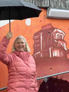 General secretary Jane Bradshaw holding an umbrella stands in front of a chalk drawing of the Goetheanum in Dornach
