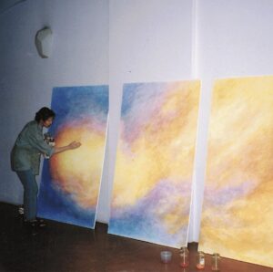 person painting a large mural on three boards leaning against a wall